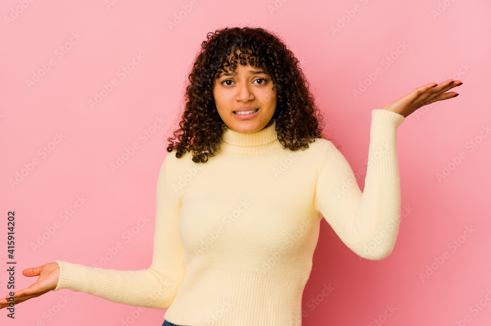 Young african american afro woman isolated confused and doubtful shrugging shoulders to hold a copy space. Young african american afro woman isolated confused and doubtful shrugging shoulders to hold a copy space.