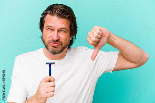 Middle age dutch man holding a razor blade isolated on blue background showing a dislike gesture, thumbs down. Disagreement concept.