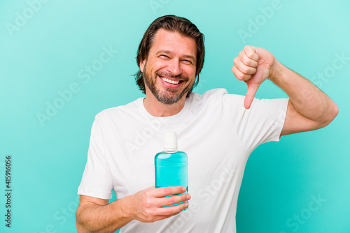 Middle age dutch man sitting holding a mouthwash isolated on blue background showing a dislike gesture, thumbs down. Disagreement concept.