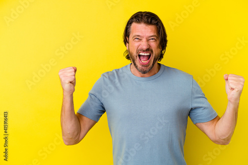 Middle age caucasian man isolated on yellow background raising fist after a victory, winner concept.