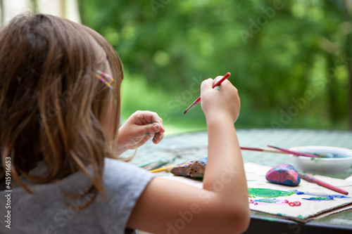 Young Girl paints Rocks outside on Patio Table