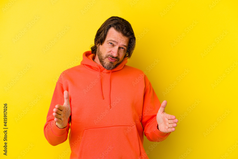 Middle age caucasian man isolated on yellow background holding something with both hands, product presentation. Middle age caucasian man isolated on yellow background holding something with both hands, product presentation.