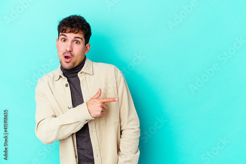 Young caucasian man isolated on blue background smiling and pointing aside, showing something at blank space.