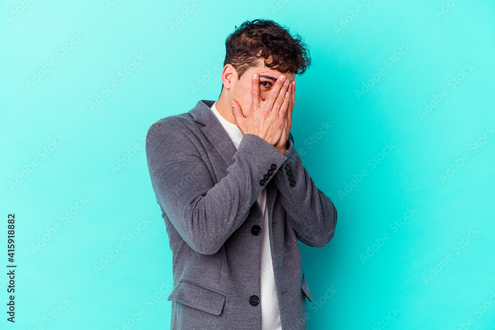 Young caucasian man isolated on blue background blink through fingers frightened and nervous. Young caucasian man isolated on blue background blink through fingers frightened and nervous.