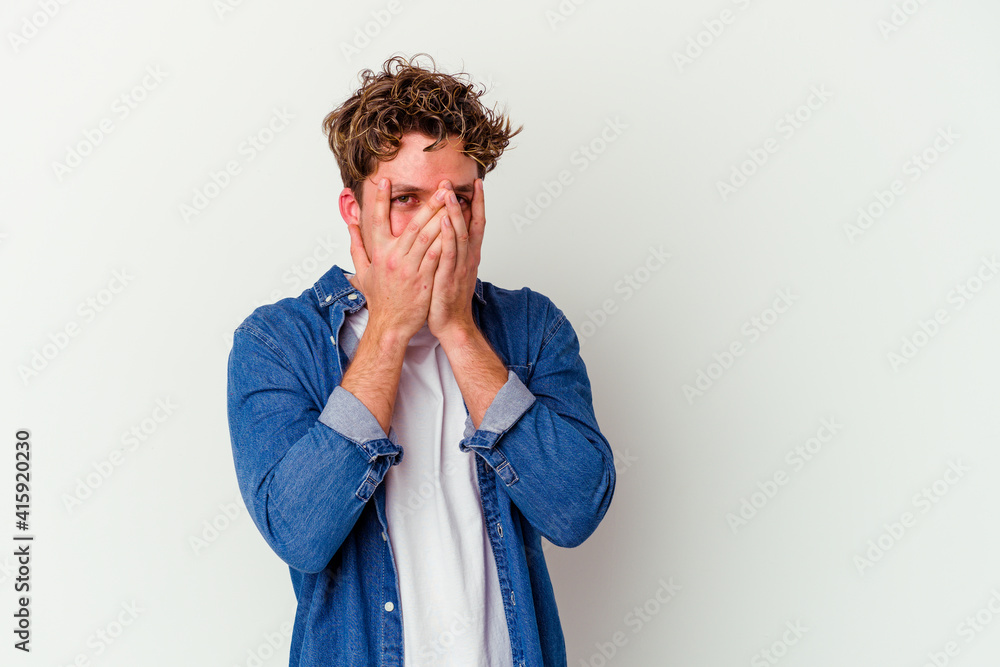 Young caucasian man isolated on white background blink at the camera through fingers, embarrassed covering face. Young caucasian man isolated on white background blink at the camera through fingers, embarrassed covering face.