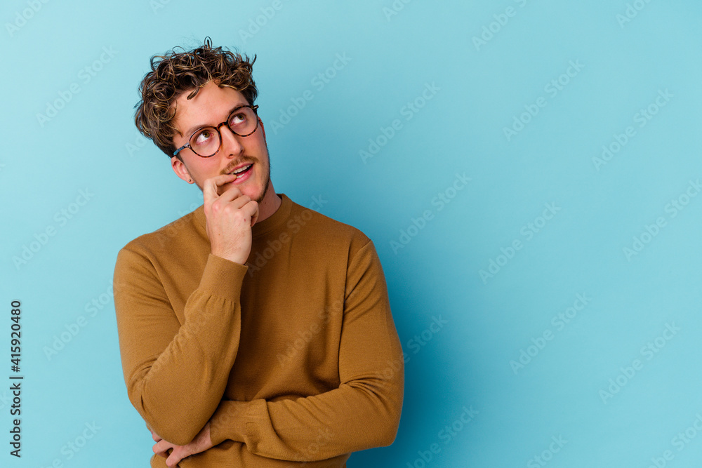 Young caucasian man wearing eyeglasses isolated on blue background relaxed thinking about something looking at a copy space.