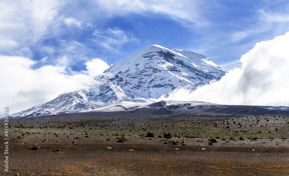 Horizontal shot of Chimborazo volcano surrounded by clouds in a blue sky. Travel in Ecuador in the Andes of South America. Horizontal shot of Chimborazo volcano surrounded by clouds in a blue sky. Travel in Ecuador in the Andes of South America.