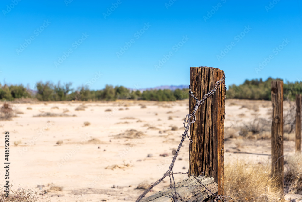 Wooden fence post with rusty barbed wire in a sandy field