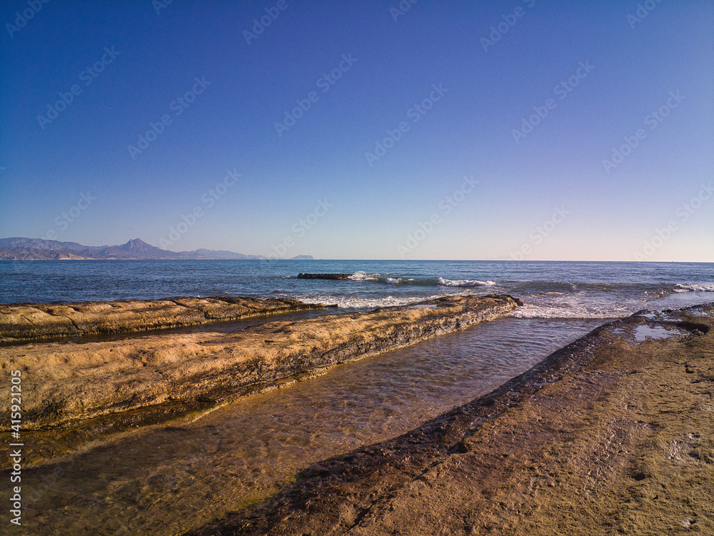 view of rocks on the beach with waves in Cabo Huertas beach in the province of Alicante, located in the Valencian Community, Spain