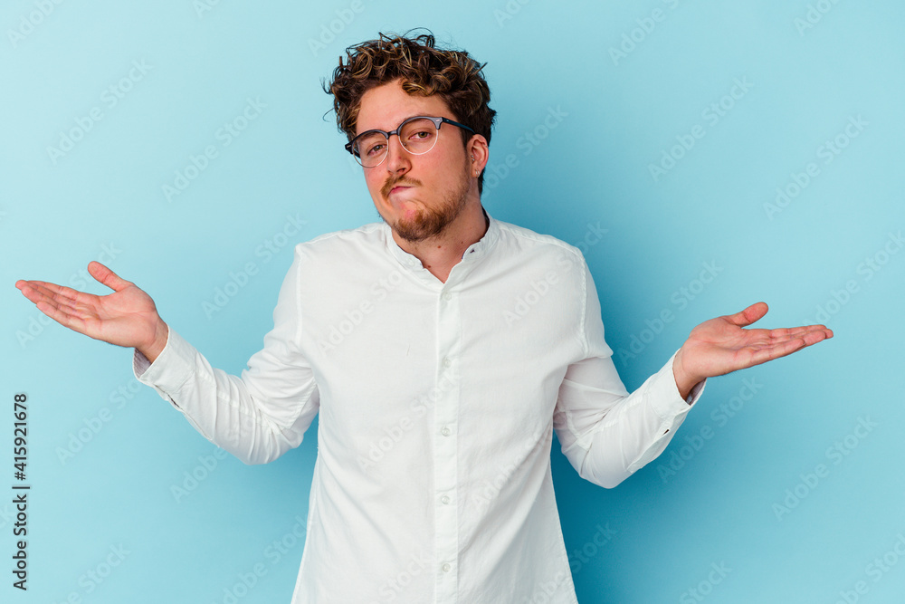 Young caucasian business man isolated on blue background doubting and shrugging shoulders in questioning gesture.