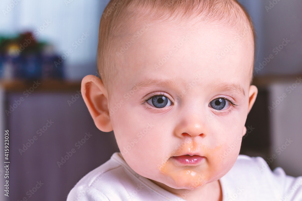 Small caucasian baby with dirty face after eating. First baby fruit puree. Close up photo of caucasian baby boy. Child learning to eat. 