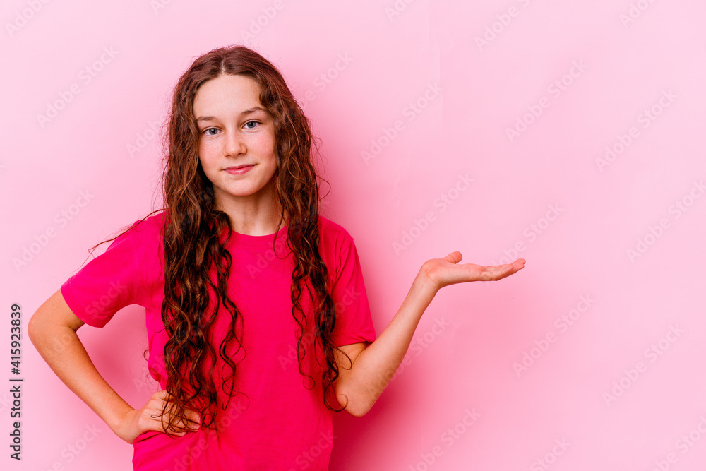 Little caucasian girl isolated on pink background showing a copy space on a palm and holding another hand on waist. Little caucasian girl isolated on pink background showing a copy space on a palm and holding another hand on waist.