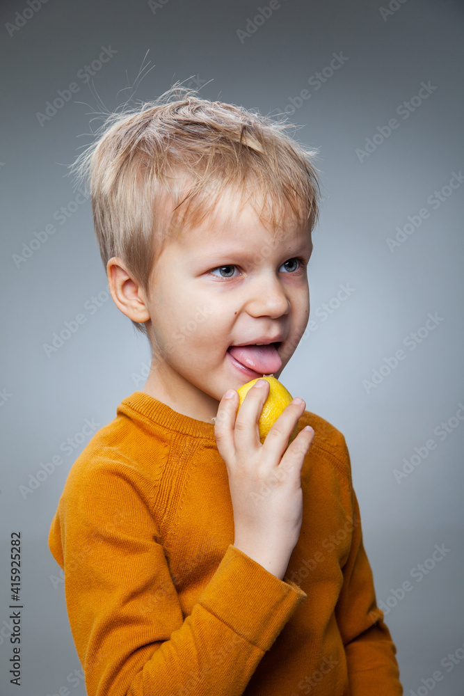 Happy child eating lemon in gray studio Happy child eating lemon in gray studio