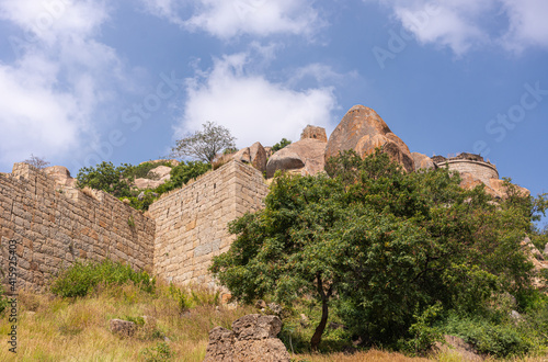 Chitradurga, Karnataka, India - November 10, 2013: Fort or Elusuttina Kote. Brown stone ramparts form corner on boulder hill with green foliage under blue cloudscape. photo