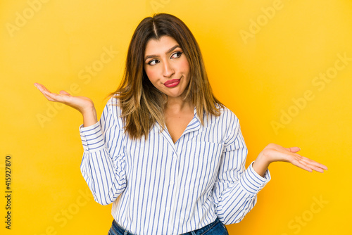 Young indian woman isolated on yellow background confused and doubtful shrugging shoulders to hold a copy space.