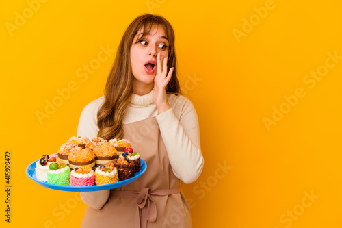 Young pastry chef woman isolated on yellow background is saying a secret hot braking news and looking aside