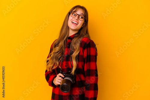 Young photographer caucasian woman isolated on yellow background looks aside smiling, cheerful and pleasant. © Asier