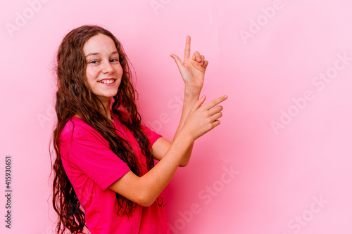 Little caucasian girl isolated on pink background excited pointing with forefingers away.