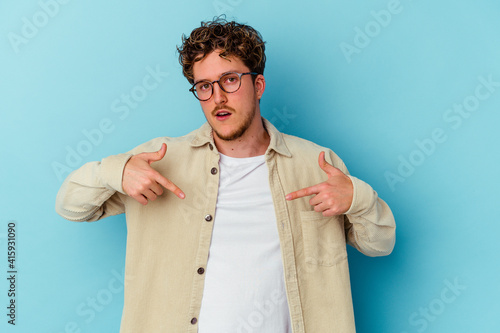 Young caucasian man wearing eyeglasses isolated on blue background points down with fingers, positive feeling.