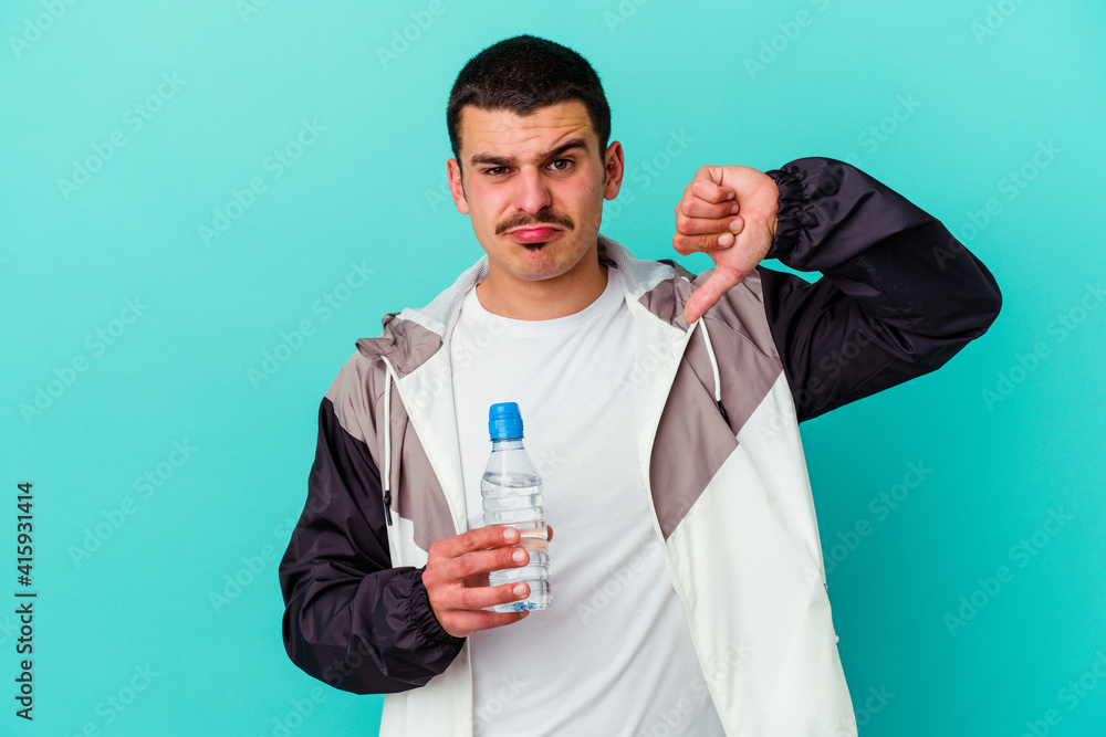 Young sporty caucasian man drinking water isolated on blue background showing a dislike gesture, thumbs down. Disagreement concept. Young sporty caucasian man drinking water isolated on blue background showing a dislike gesture, thumbs down. Disagreement concept.