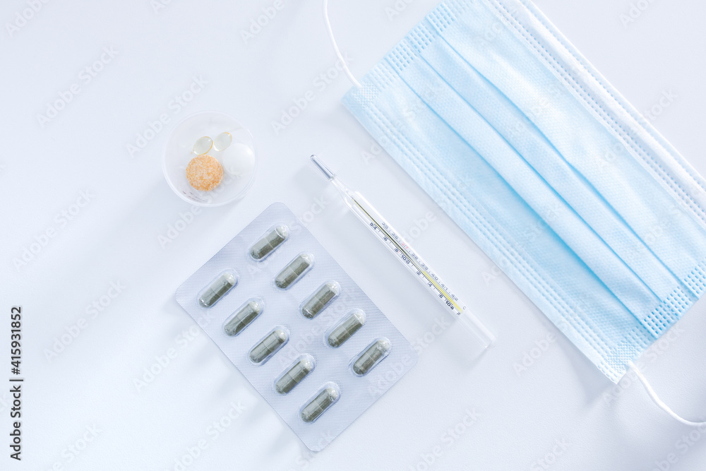 Medical objects on white background new surgical face mask, unused thermometer, strip pack of capsule and immune vitamins tablets to protection from spreading of virus pandemic and prevention disease Medical objects on white background new surgical face mask, unused thermometer, strip pack of capsule and immune vitamins tablets to protection from spreading of virus pandemic and prevention disease