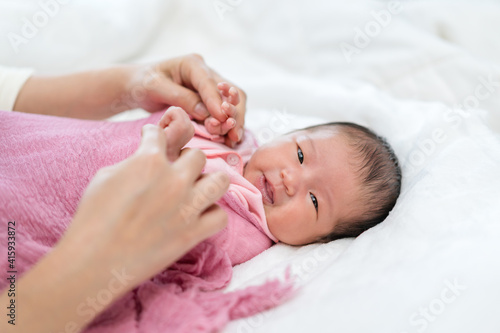happy newborn baby wrap in blanket and parent hands on bed