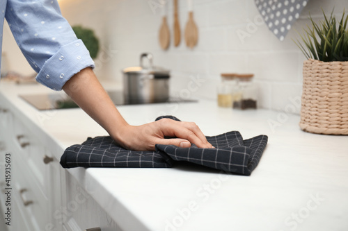 Woman wiping white table with kitchen towel, closeup