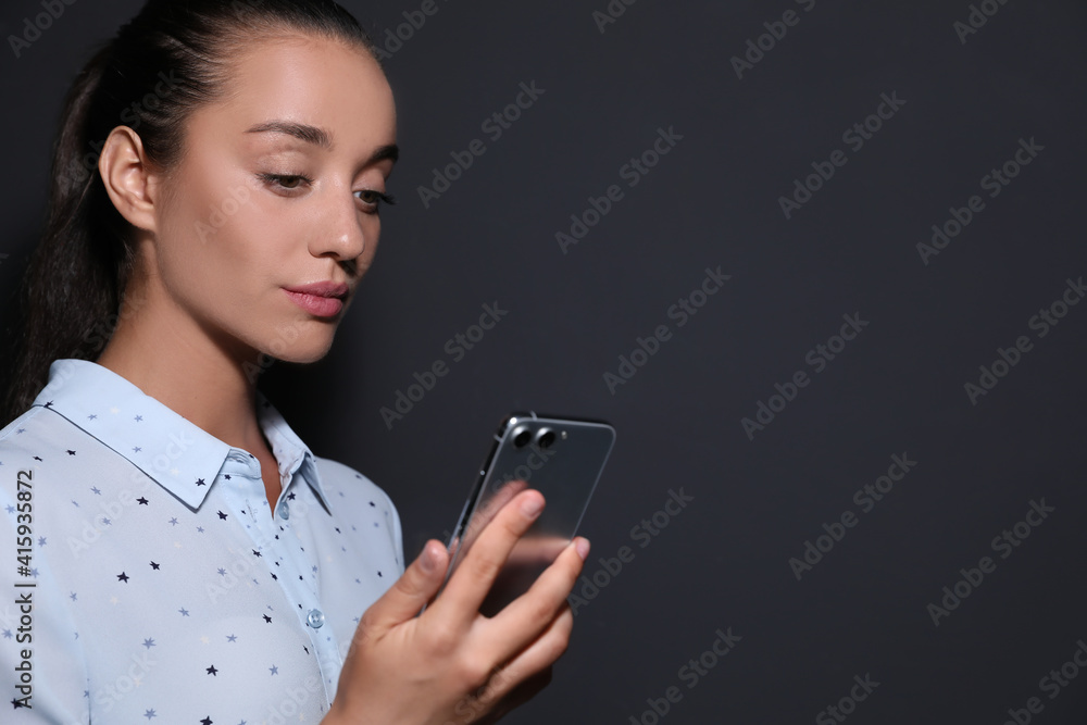 Young woman unlocking smartphone with facial scanner on black background, space for text. Biometric verification