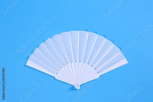 White hand fan on light blue background, top view