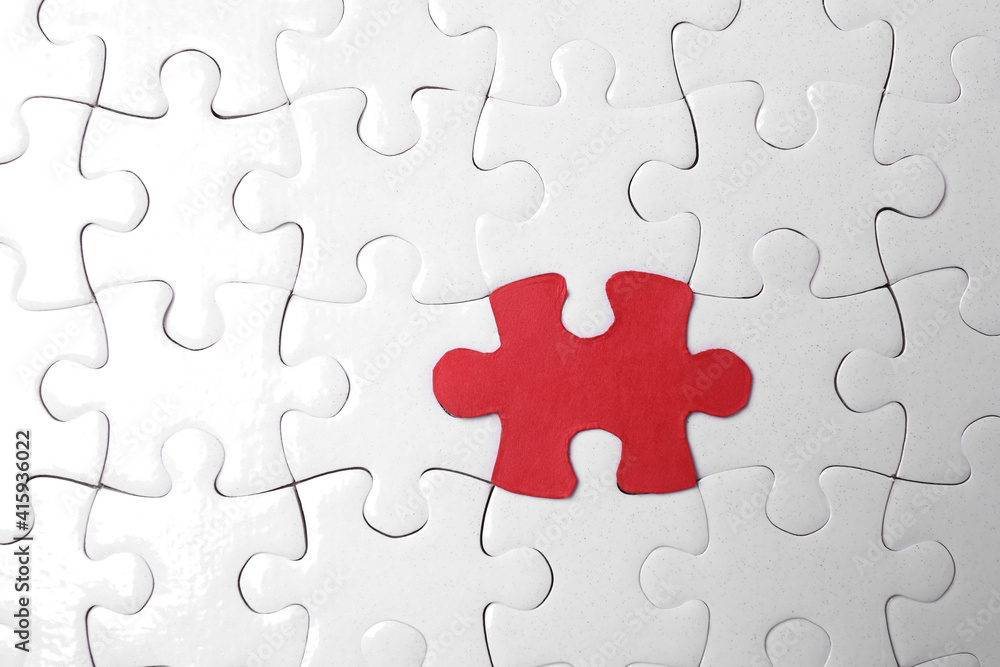 White jigsaw puzzles and red one as background, top view