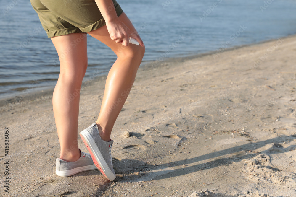 Woman applying insect repellent onto leg at beach, closeup. Space for text