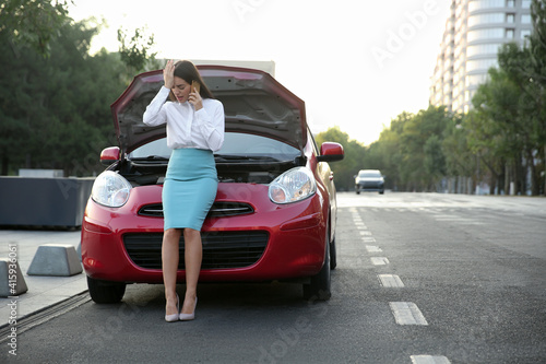 Stressed woman talking on phone near broken car outdoors © New Africa