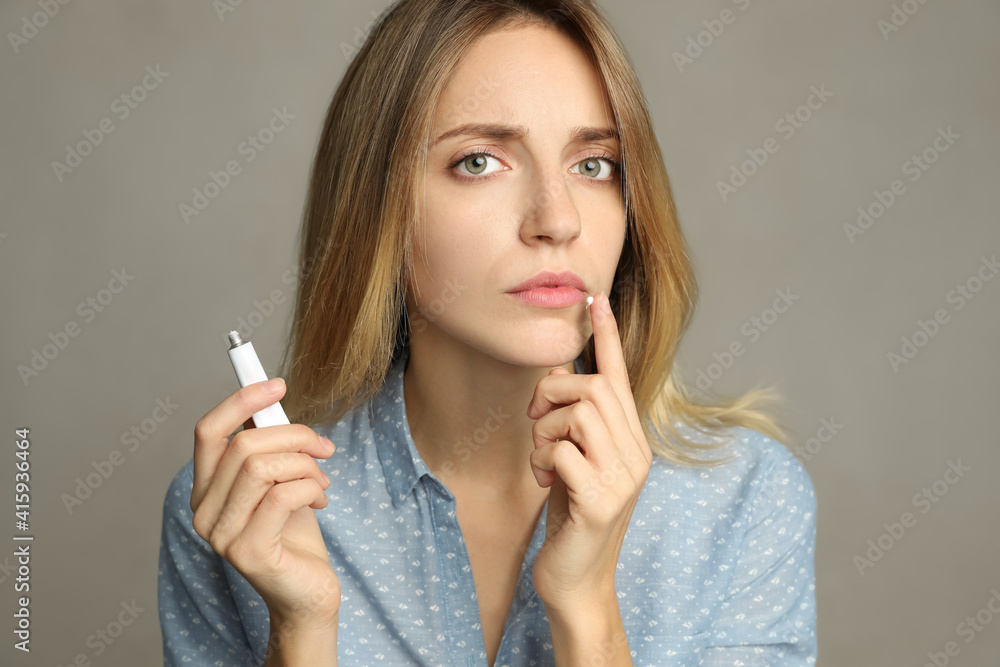 Obraz premium Woman with herpes applying cream onto lip against light grey background
