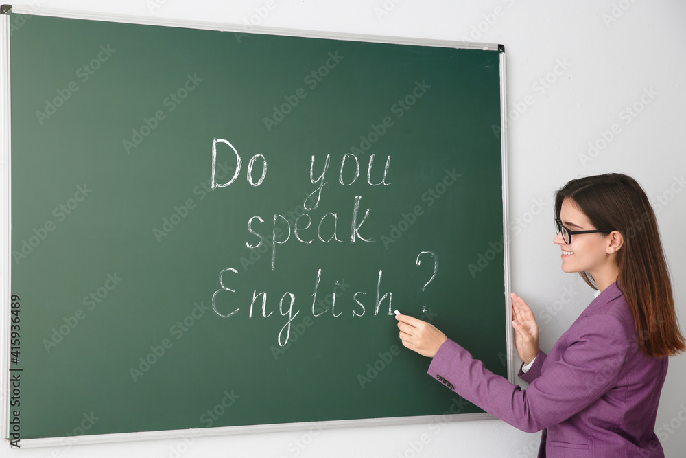 Teacher near green chalkboard with words Do You Speak English?