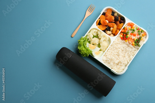 Thermos and lunch box with food on light blue background, flat lay. Space for text
