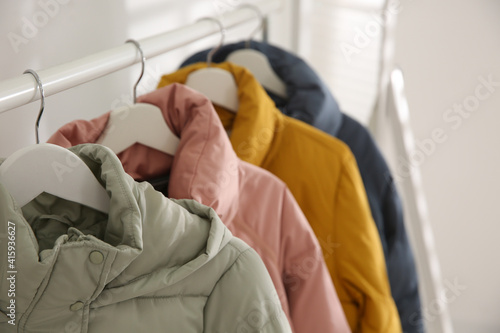 Different warm jackets hanging on rack indoors, closeup photo