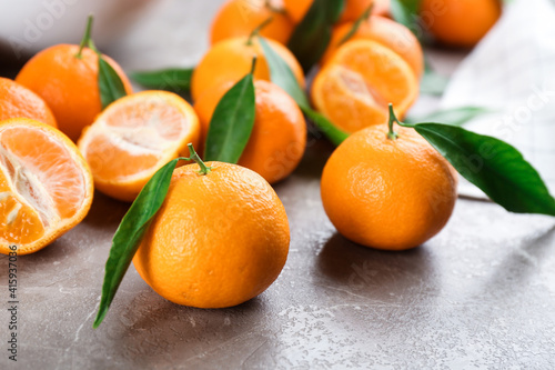 Fresh tangerines with green leaves on grey table, closeup