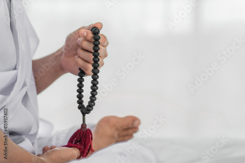 black rosary beads in hand of religious buddhist man in white clothing having sitting and rosary count meditation