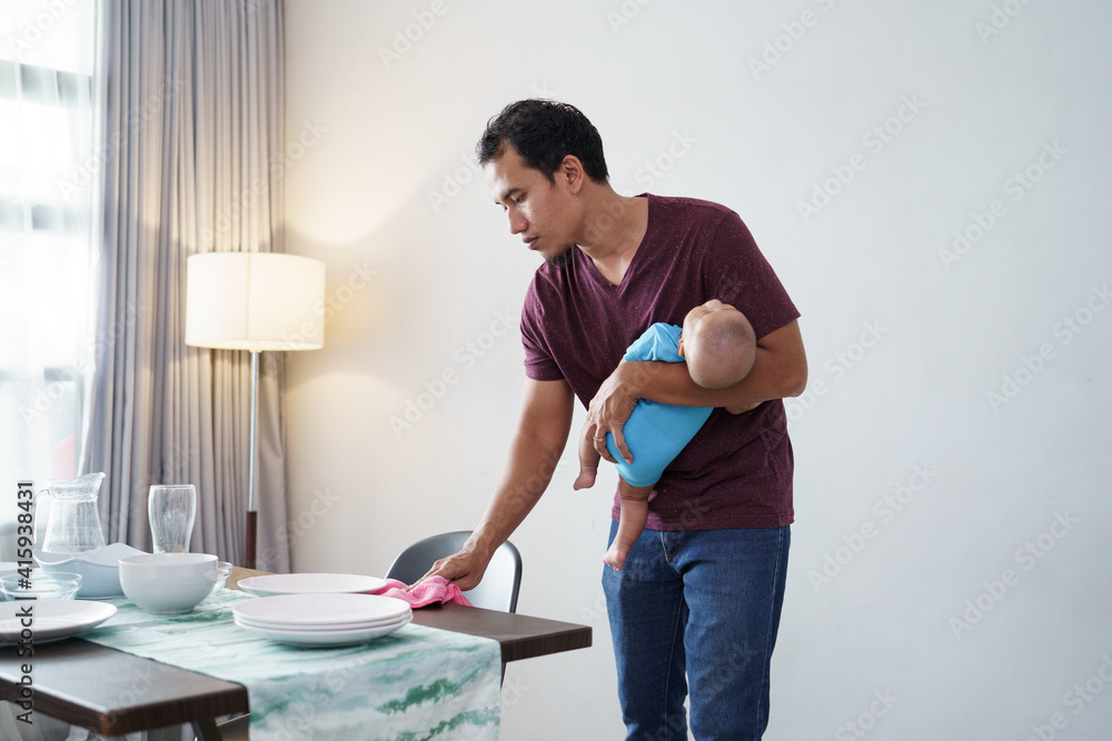 portrait of single father doing chores at home while carrying his baby portrait of single father doing chores at home while carrying his baby