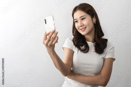 A young beautiful Asian woman with long hair smiling uses a cell phone for a selfie, chatting, or social media. On white background in studio. Online technology, online shopping concept. Copy space