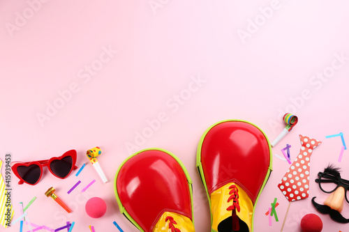 Flat lay composition with clown shoes and accessories on pink background. Space for text