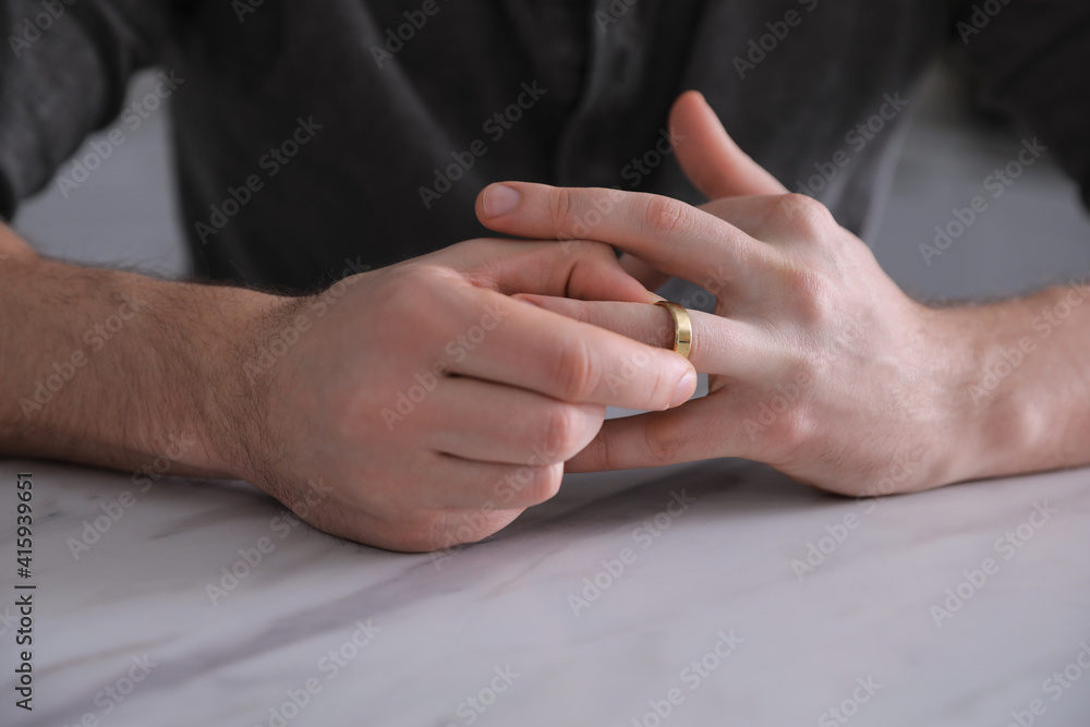 Fototapeta premium Man taking off wedding ring at white marble table, closeup. Divorce concept