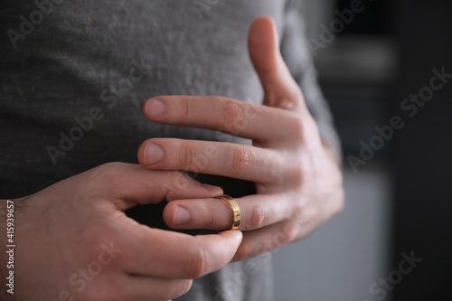 Man taking off wedding ring on blurred background, closeup. Divorce concept photo