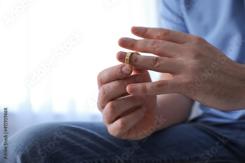 Man taking off wedding ring on blurred background  closeup. Divorce concept