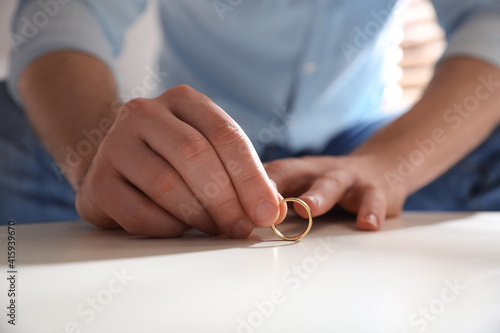 Man with wedding ring at table indoors, closeup. Divorce concept