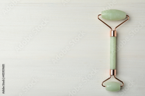 Natural jade face roller on white wooden background, top view. Space for text