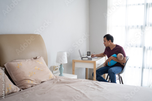 portrait of a busy father working from home while holding his infant baby
