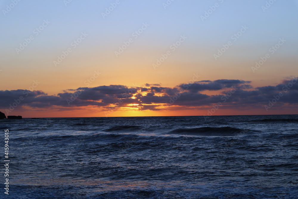 Beautiful New Zealand orange sunset with scattered clouds and ocean and waves Beautiful New Zealand orange sunset with scattered clouds and ocean and waves