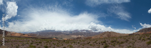 Panorama view of the arid desert, brown land and rocky mountains under a beautiful blue sky with clouds. 