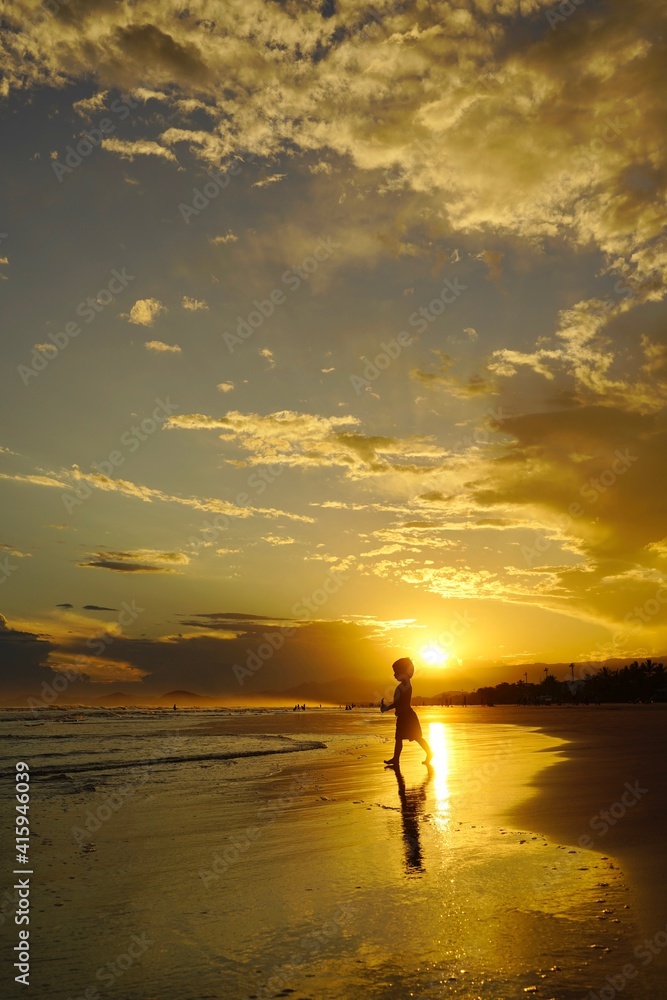 Por do sol na praia com a sombra de um garoto caminhando em direção ao mar 